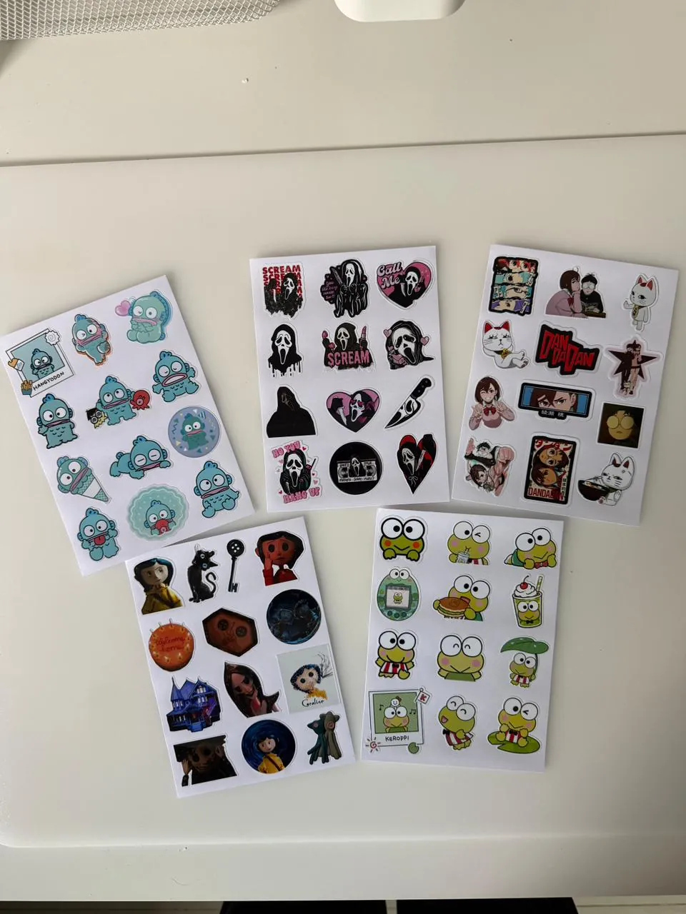 Cinco planillas de stickers: Hangyodon, Scream, Dan Da Dan, Coraline y Keroppi